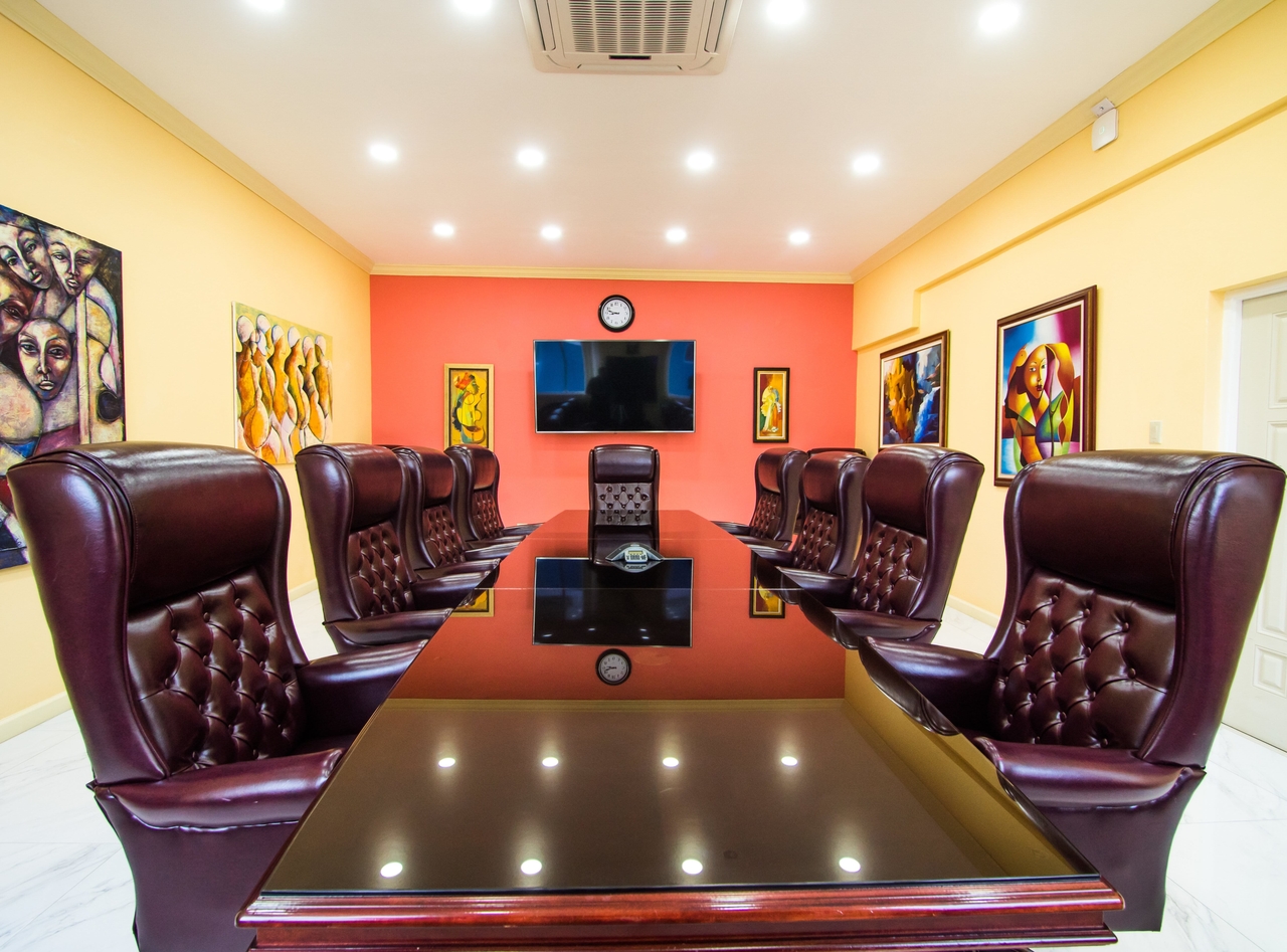 Shot of Hylton & Hylton's conference room. 10 burgundy conference chairs are placed around a large rectangular conference room table with beautiful paintings around the room